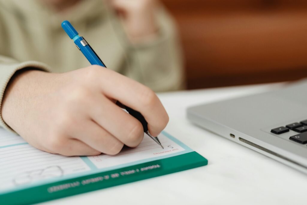 A close shot of a hand writing on a notepad near a laptop, suitable for productivity concepts.